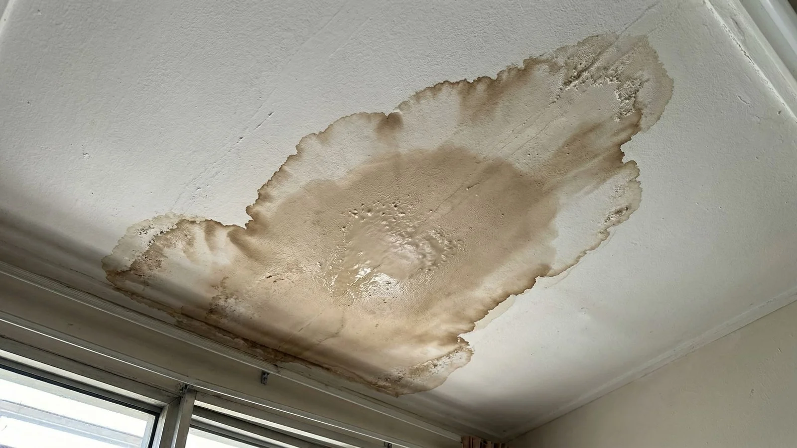 Brown water stain on a white ceiling indicating a roof leak in a Malaysian home